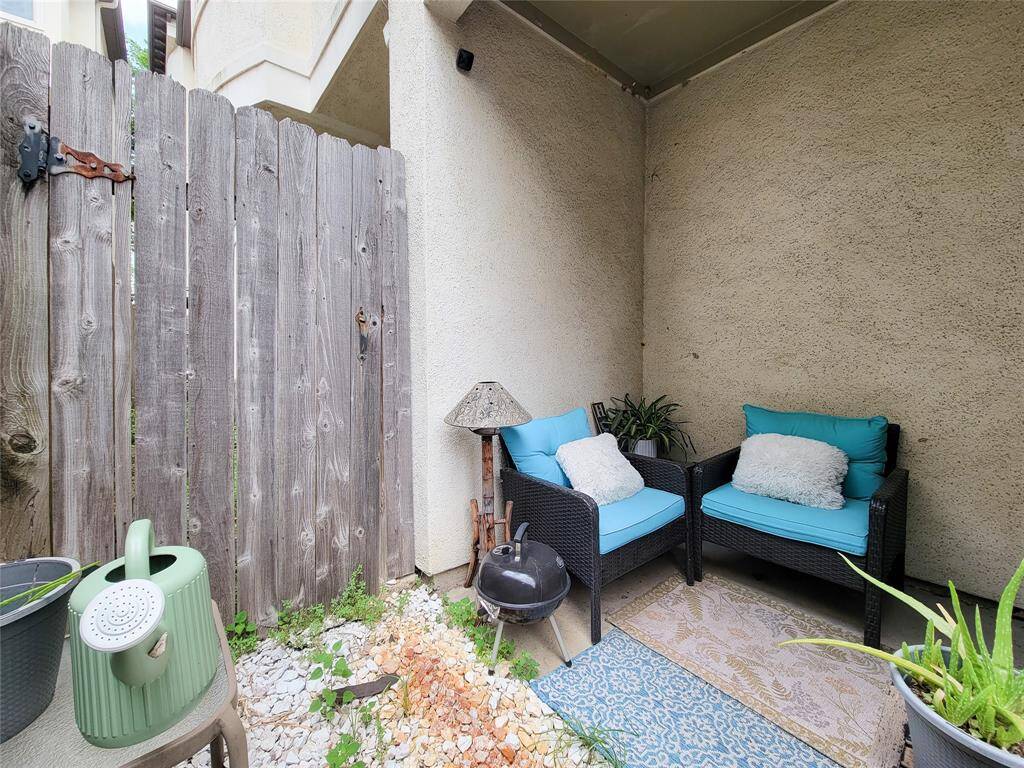 Cozy outdoor patio with two wicker chairs and blue cushions, perfect for relaxation. The space is accented with a small lamp, plants, and a rustic wooden fence for privacy. Ideal for intimate gatherings or a quiet retreat.