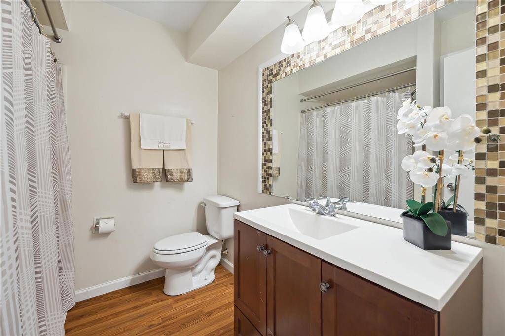 This bathroom features a modern design with a stylish vanity, a large mirror with mosaic tile accents, and a clean, neutral color palette. It includes a shower with wooden flooring, creating a warm and inviting space.