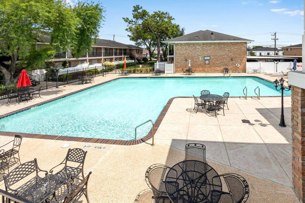 The spacious outdoor pool area with surrounding patio space, featuring multiple tables and chairs for relaxation. The area is well-maintained and the mature trees provide a nice breeze and plenty of shade offering an inviting space for leisure and for entertaining.