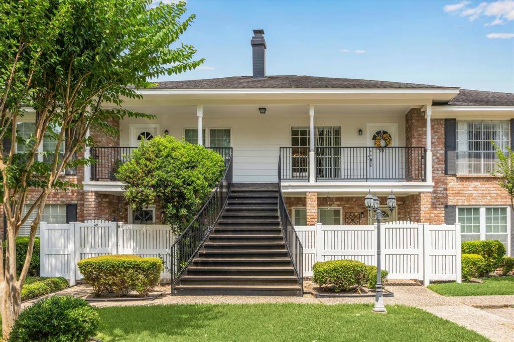 This photo showcases a charming brick condo with a welcoming front porch, accessible by a central staircase. The exterior features well-maintained landscaping, white fencing, and a classic lamp post, creating a cozy, inviting atmosphere.