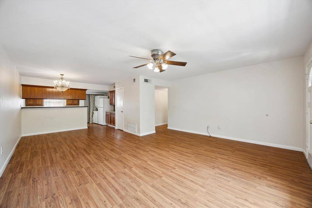 This view showcases the spacious living and dining room areas with the open layout leading to the kitchen. The kitchen boasts wooden cabinetry, a breakfast bar, and a chandelier, providing a cozy and inviting atmosphere.