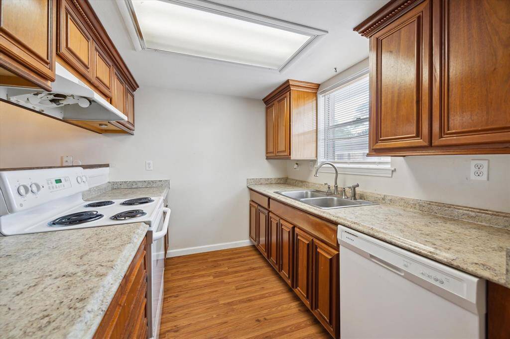 This kitchen features wooden cabinetry, granite countertops, white appliances (electric stove and dishwasher) double sink, and natural light from your kitchen window.