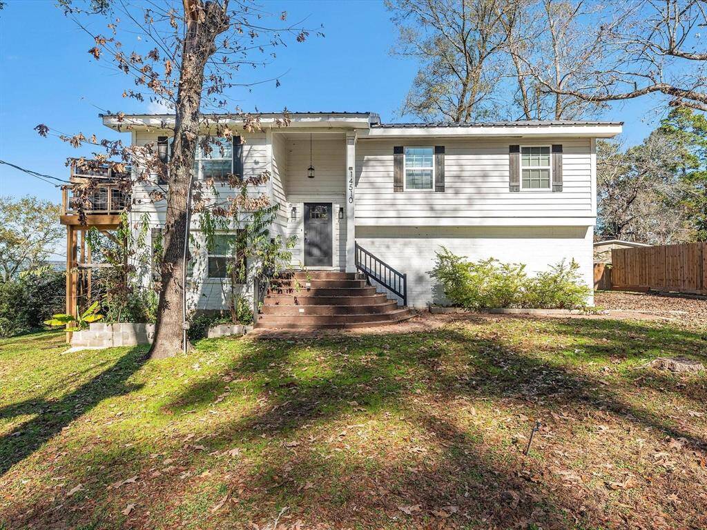 Charming two-story home with a white exterior and inviting front steps. Surrounded by mature trees and greenery, it features a wooden deck on the side and a spacious yard, offering a serene, natural setting.