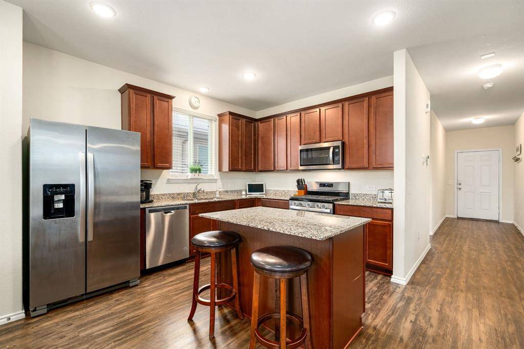 Spacious kitchen featuring rich wood cabinetry, granite countertops, and stainless steel appliances. A center island with seating offers extra prep space and casual dining, all set against durable wood-look flooring and soft recessed lighting.