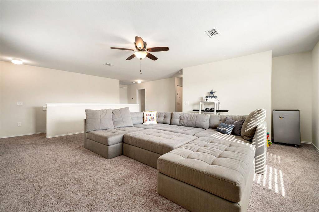 Expansive upstairs game room with plush carpet, neutral tones, and ample space for lounging or entertaining. Natural light fills the room, complemented by a ceiling fan for added comfort.