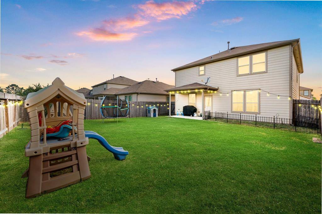 Expansive backyard perfect for entertaining or play, complete with a covered patio, string lighting, and plenty of green space. Features a playset and trampoline, ideal for family fun. Fully fenced for privacy and peace of mind. No back neighbors.