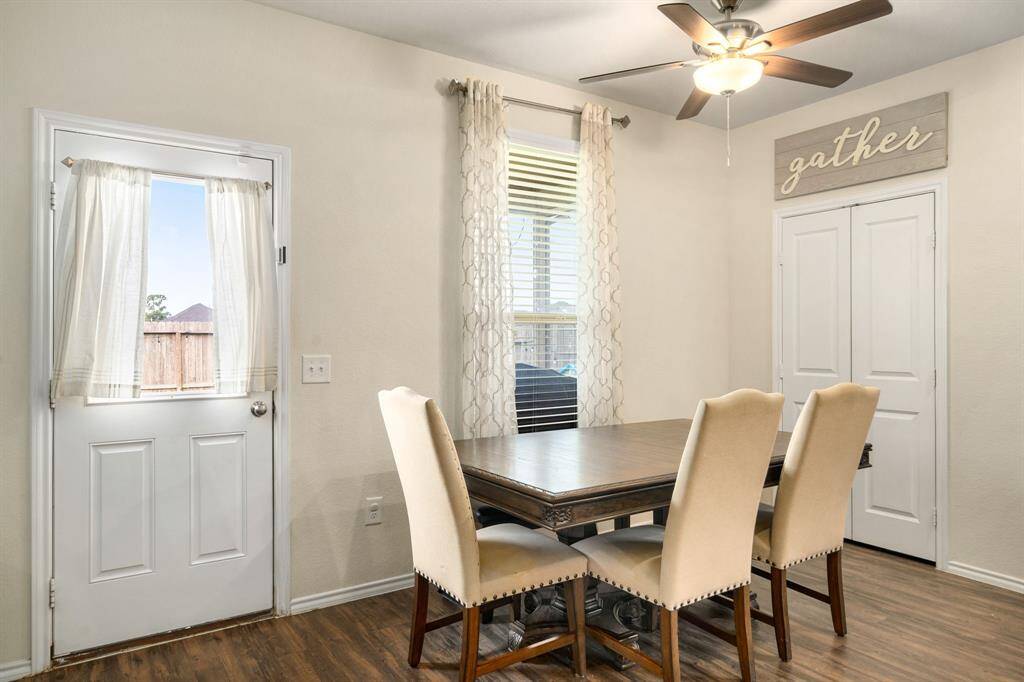 Bright and inviting dining area featuring wood-style flooring, a ceiling fan, and direct access to the backyard. A large window and neutral finishes create a warm space ideal for everyday meals or hosting guests.