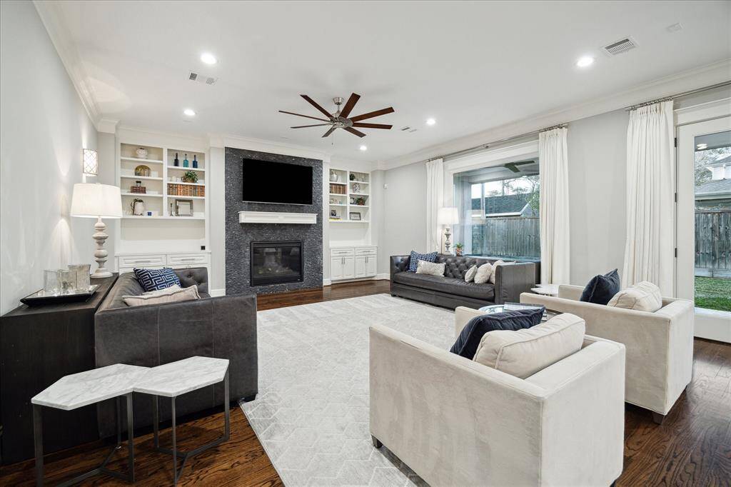 The open concept living area overlooks the backyard with covered patio and outdoor kitchen.  It features gas log fireplace flanked with custom built-ins, high ceilings, hardwood floors, designer ceiling fan, recessed lighting, wall sconces, and crown molding.