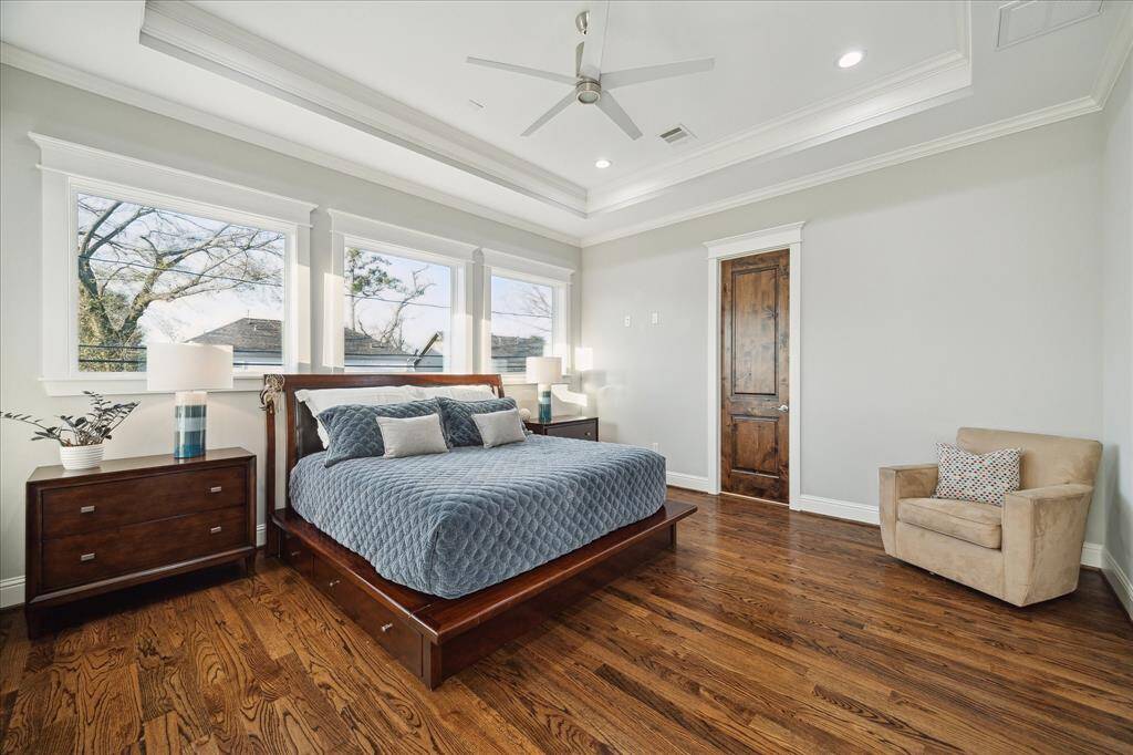 A sun filled primary suite is privately situated upstairs off the back of the home and features a tray ceiling, hardwood floors, designer ceiling fan, recessed lighting, and crown molding.