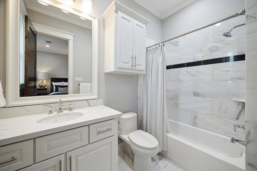 This is the ensuite bath for guest bedroom 1 which includes a spacious vanity, quartz counters, tub/shower combo with natural stone surround, and natural stone tile floors.