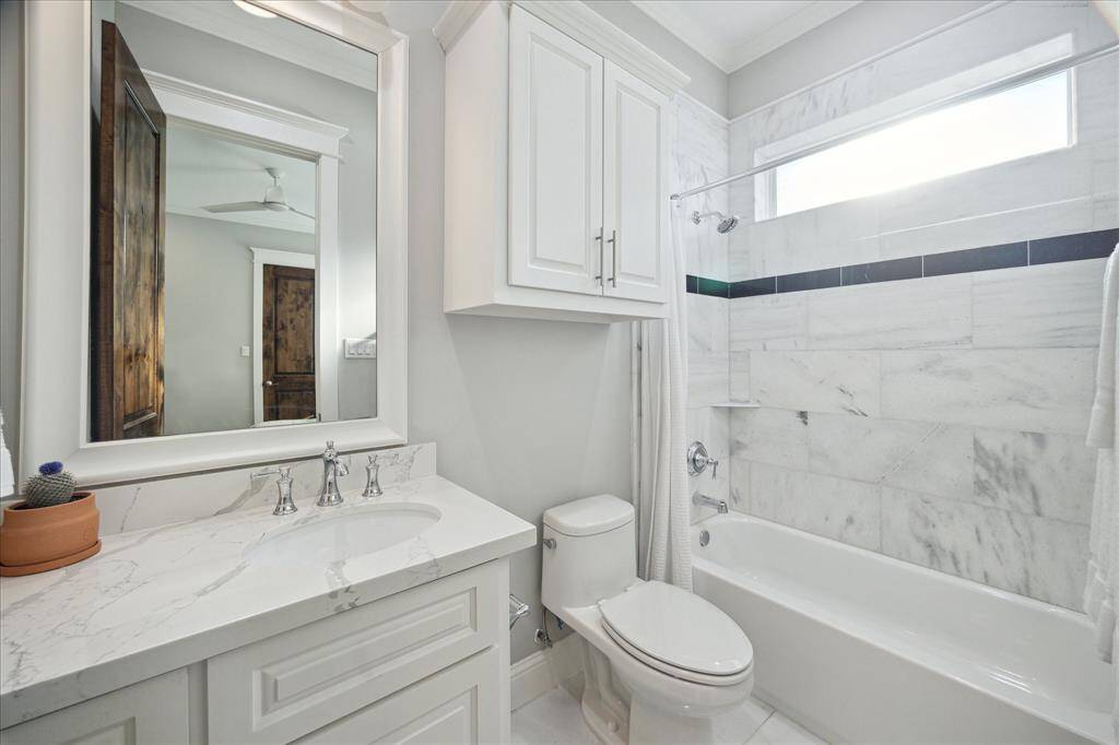 This is the ensuite bath for guest bedroom 3 which includes a spacious vanity, quartz counters, tub/shower combo with natural stone surround, and natural stone tile floors.