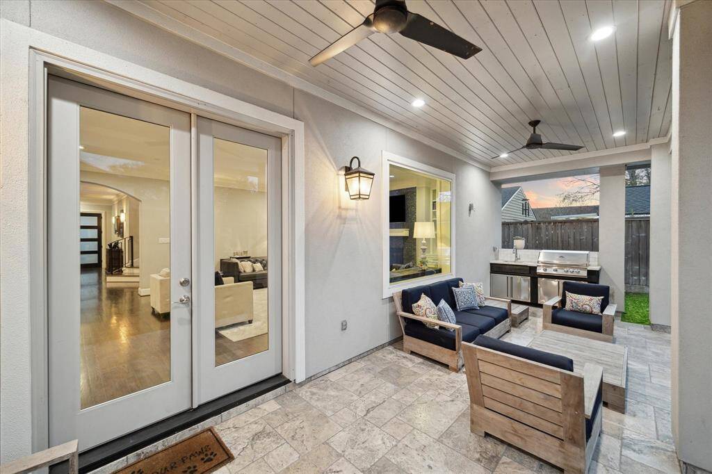 The covered patio features two ceiling fans, recessed lighting, natural stone floors, and an outdoor kitchen with built-in gas grill and a sink.