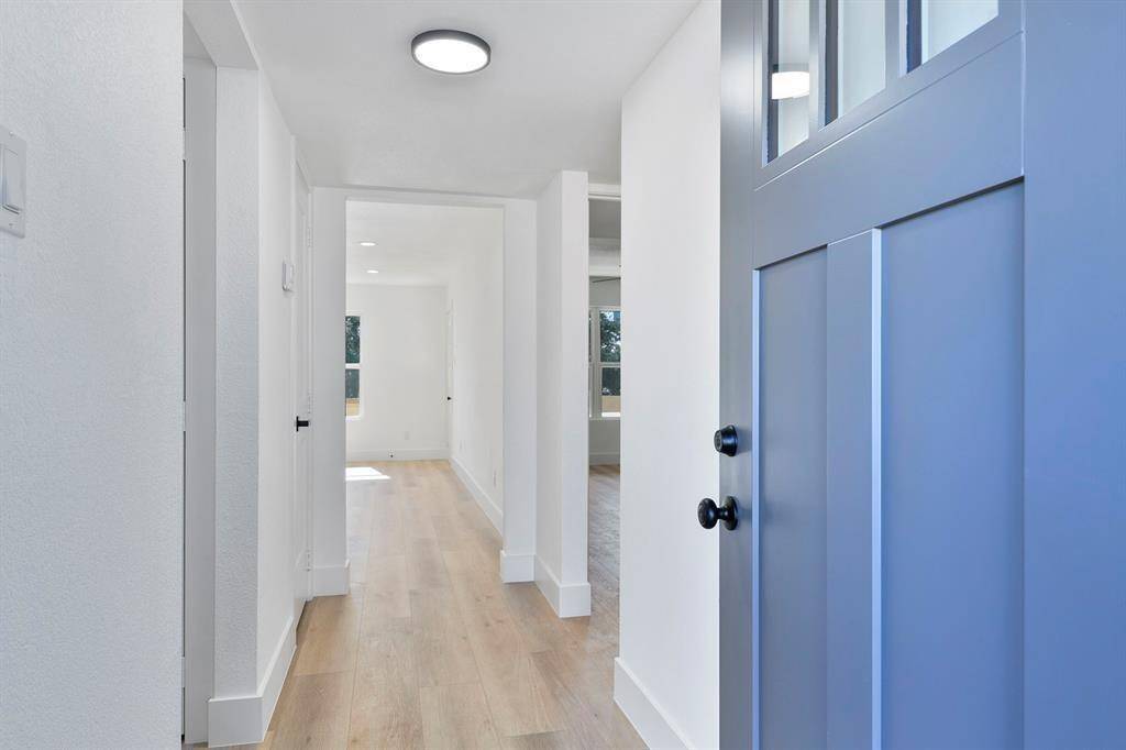 Bright and inviting entrance with a modern blue door, light hardwood floors, and white walls. The hallway leads to a well-lit living area, creating an open and airy feel.