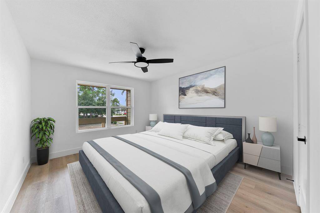This photo showcases a bright, modern bedroom with a large window offering natural light. It features a comfortable bed, stylish artwork, and a ceiling fan, complemented by light wood flooring and neutral walls.