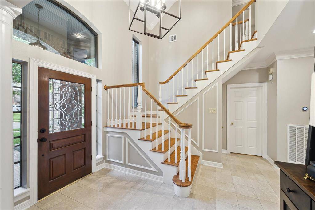 The foyer features a beautiful front door with leaded glass inserts, elegant tiled flooring, and a pretty stairway with wood stair treads.
