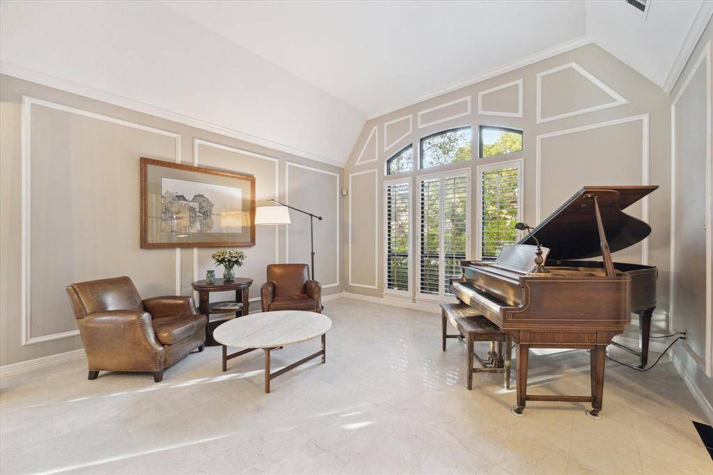 The elegant living room features high ceilings, picture frame molding, large windows with plantation shutters, and abundant natural light, creating an inviting space.