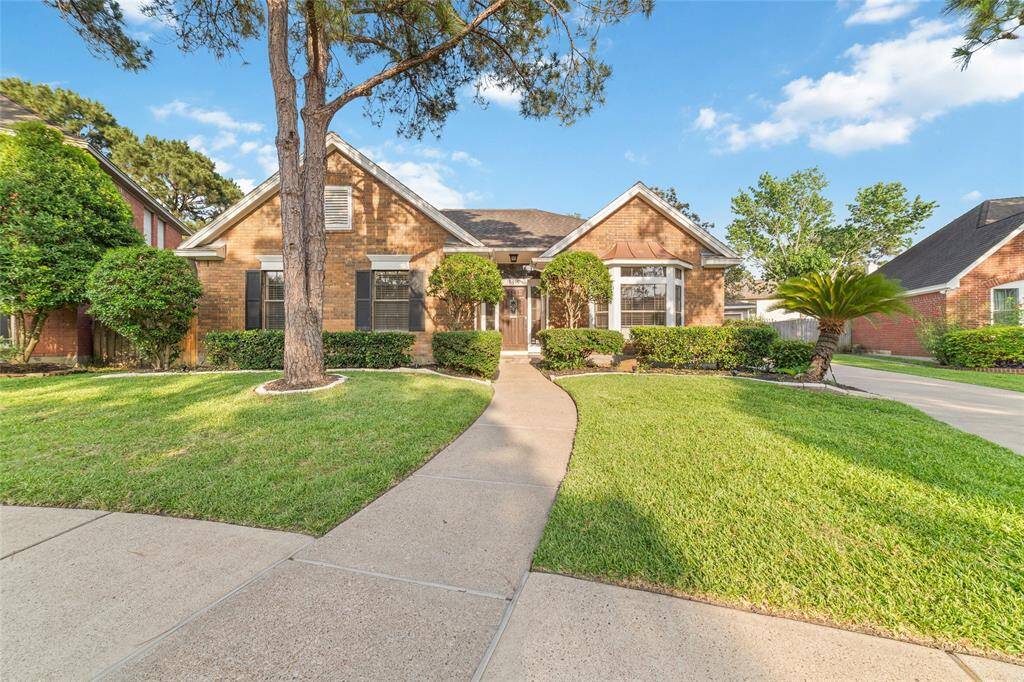 This inviting home features a charming brick exterior with a well-maintained front yard. A curved walkway leads to the entrance, flanked by manicured shrubs and mature trees, creating a welcoming atmosphere.