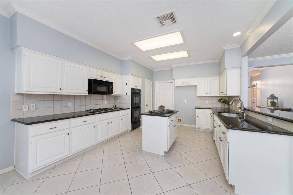 Spacious and bright kitchen featuring white cabinetry, granite countertops, and a central island. Equipped with modern appliances, tile flooring, and plenty of overhead lighting. Perfect for cooking and entertaining.