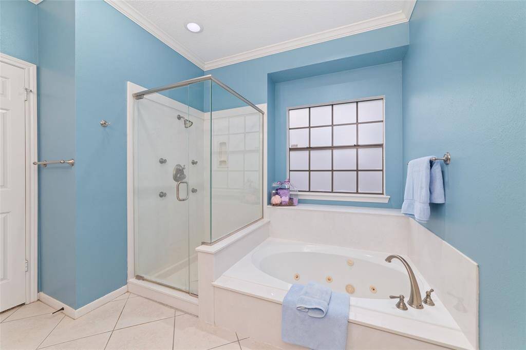 This bathroom features a large glass-enclosed shower and a separate corner bathtub with jets. The walls are painted a calming blue, complemented by a frosted window for natural light and privacy.