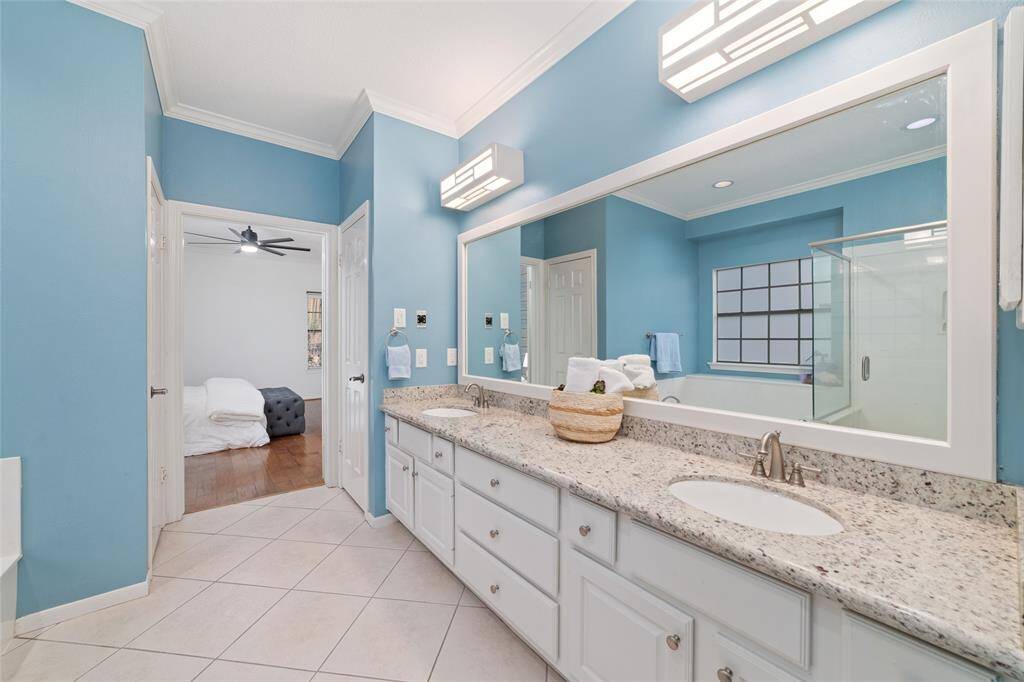 This bathroom features a spacious double vanity with granite countertops, modern lighting, and ample storage. The blue walls add a refreshing touch, and the room includes a glass-enclosed shower. It connects to a bedroom with hardwood flooring, offering a seamless and stylish layout.