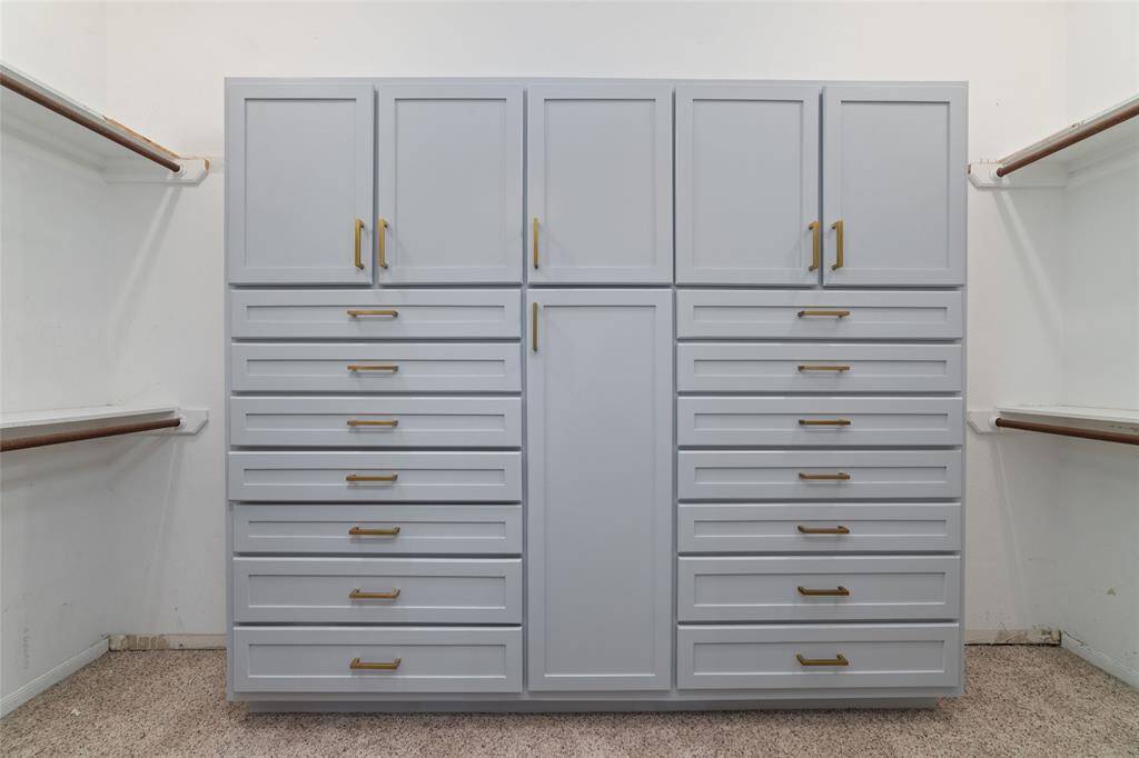 This photo shows a spacious walk-in closet featuring elegant built-in cabinetry with multiple drawers and cabinets, complemented by ample hanging space on both sides.