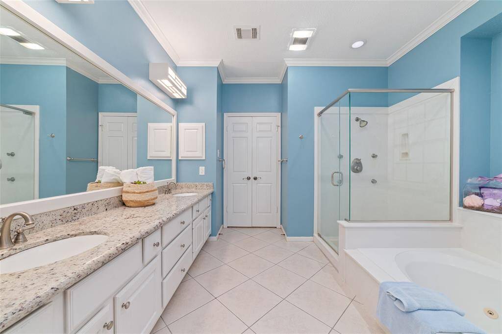 This bathroom features a spacious layout with a dual-sink vanity and granite countertops. It has a glass-enclosed shower and a separate bathtub. The walls are painted in a soothing blue, and there's ample cabinet storage, creating a serene and functional space.