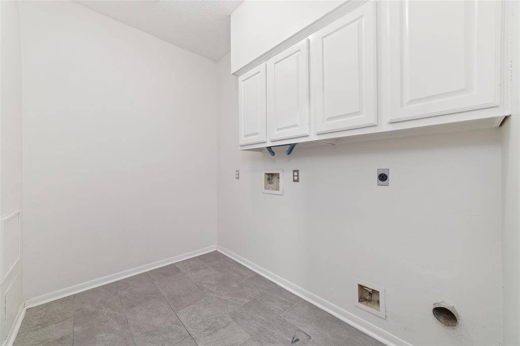 This photo shows a utility room with white walls and tile flooring. It features overhead storage cabinets and connections for a washer and dryer, providing a functional space for laundry tasks.