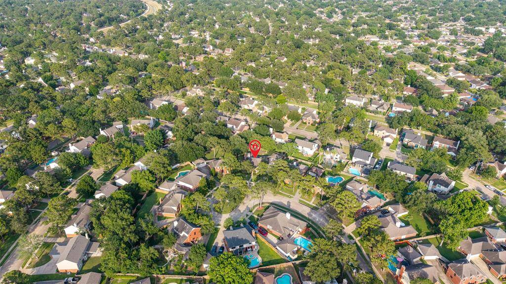 This aerial photo showcases a lush, tree-filled suburban neighborhood with winding streets and well-spaced homes, many featuring pools. It's a peaceful, green area ideal for families seeking community living.