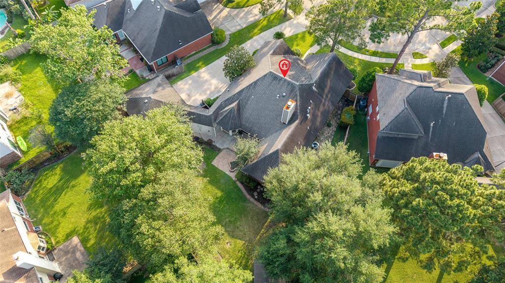 This aerial view showcases a charming home with a spacious, tree-lined yard in a peaceful residential neighborhood. The property is surrounded by well-maintained homes and lush greenery, offering a serene and inviting atmosphere.