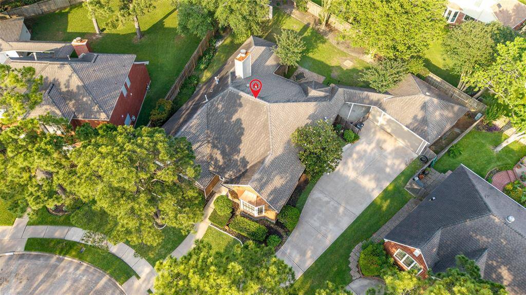 This aerial view showcases a spacious suburban home with a large driveway, surrounded by lush greenery. The property is situated in a quiet neighborhood with well-maintained yards and mature trees, offering privacy and a serene environment.