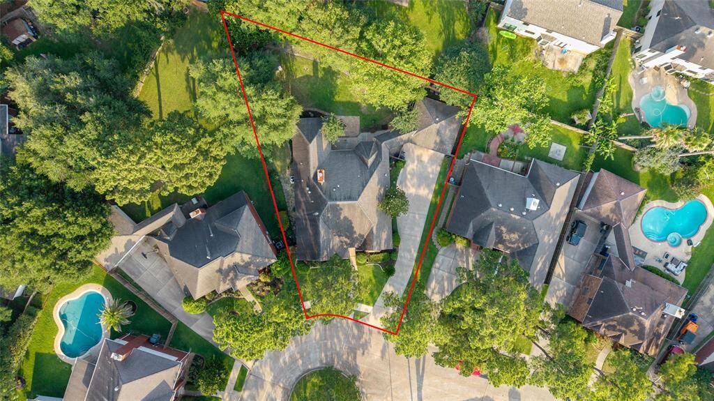 This aerial photo showcases a spacious home within a red boundary, situated in a lush, tree-lined neighborhood. The property is part of a cul-de-sac, offering privacy and reduced traffic. Nearby homes feature swimming pools, highlighting a family-friendly, upscale area.