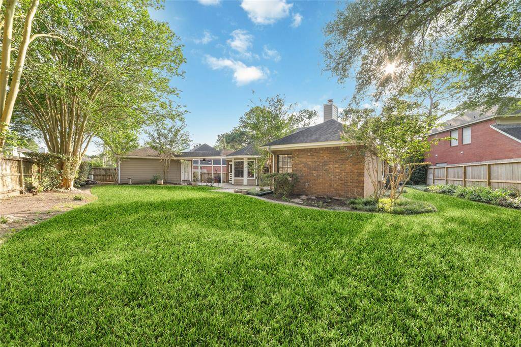 Spacious backyard with lush green grass, mature trees, and a cozy brick house. The area is fenced, offering privacy and ample space for outdoor activities.