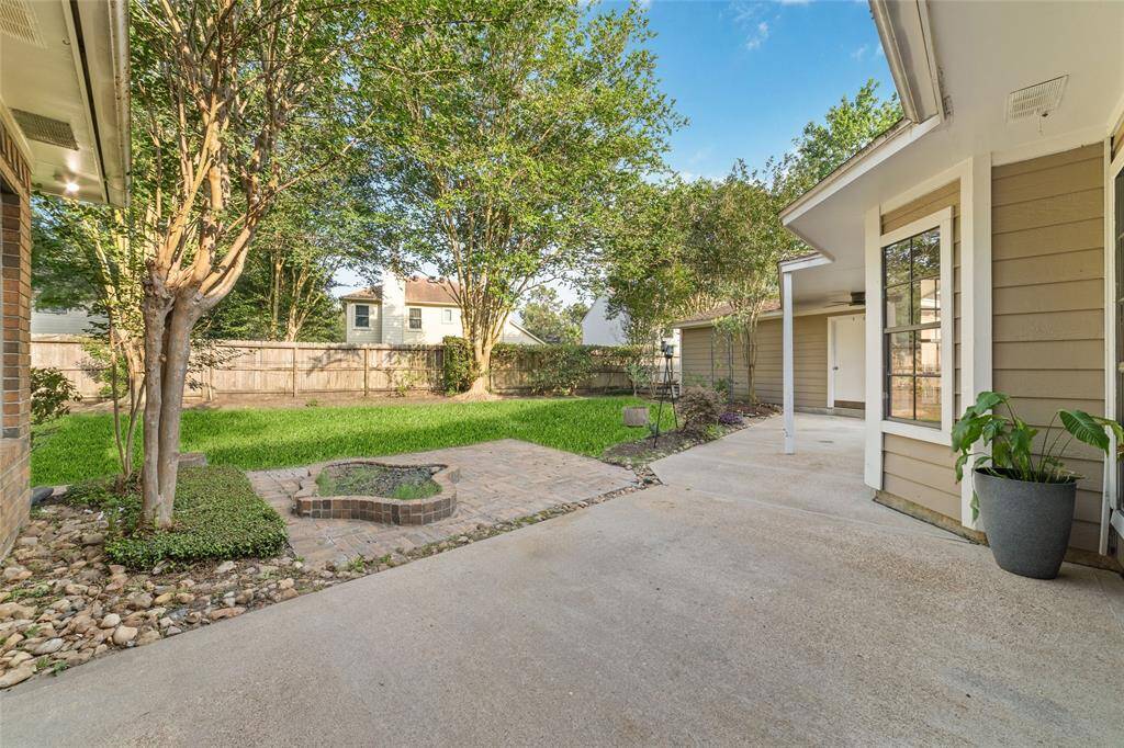This backyard features a spacious patio with a paved area and a built-in fire pit, surrounded by a well-maintained lawn and mature trees, perfect for outdoor gatherings.
