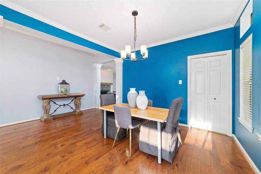 This dining area features vibrant blue accent walls, hardwood flooring, and a modern light fixture. It includes a cozy wooden table with upholstered chairs and a decorative console table. Natural light streams through a nearby window, enhancing the bright and welcoming atmosphere.