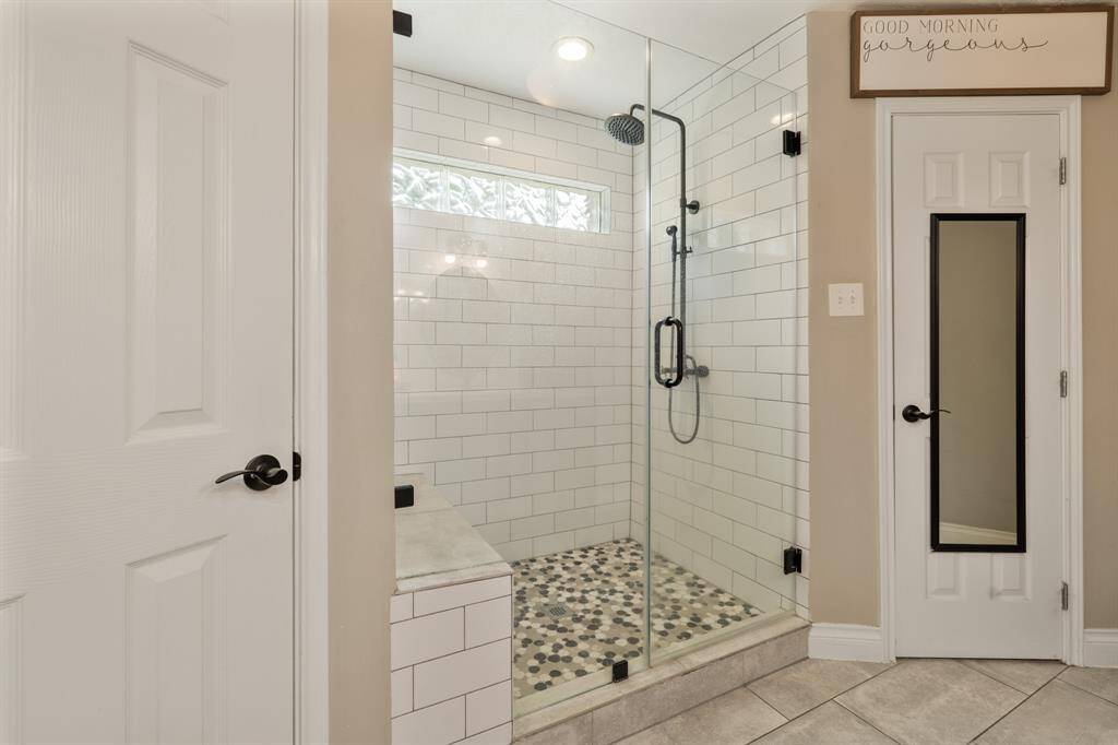 The primary bathroom has an oversized walk-in shower with tile surround, mudset flooring, frameless glass entry, and modern plumbing fixtures.