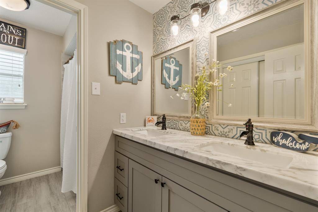 Located just off the secondary bedrooms, this fully remodeled bathroom offers additional privacy with separated vanity and shower making it easy to share and get ready. It features with gray cabinets, quartz countertops, framed mirrors, and accent tiled wall.