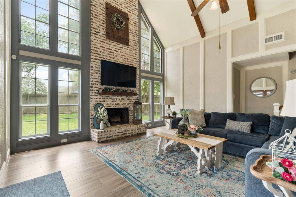 Warm and inviting, this stunning living space features a cozy fireplace with brick surround extended to the ceiling, creating the perfect ambiance for relaxation. Expansive windows flood the room with natural light and gives peaceful backyard views through grand windows, all framed by elegant wood beams and stylish finishes throughout.