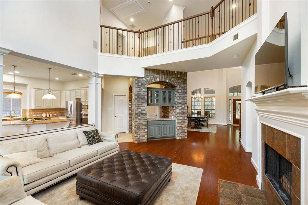 This angle showcases the open-concept flow from the living room into the bright kitchen and breakfast area, perfect for everyday living and entertaining. Just beyond the arched brick accent wall is the dining room, while the door to the left leads to a spacious laundry room and access to the garage. The layout offers both functionality and charm, with soaring ceilings, warm wood flooring, and architectural details that tie the spaces together beautifully.