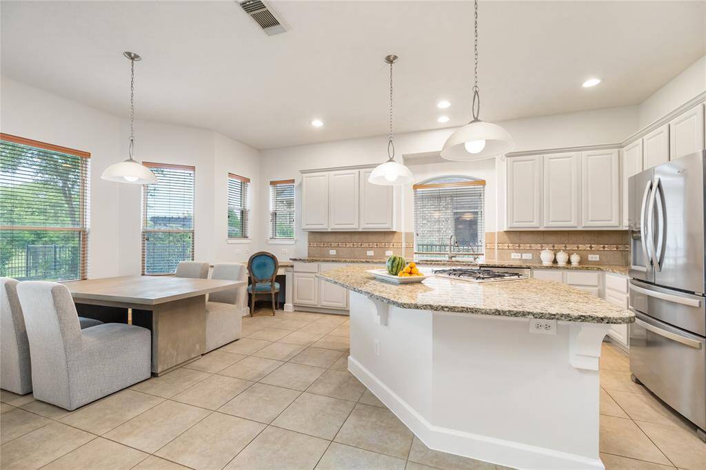 This bright and airy kitchen is the heart of the home, featuring granite countertops, a spacious island with gas cooktop, stainless steel appliances, and abundant cabinet storage. Pendant lighting adds a stylish touch, while the adjoining breakfast area is surrounded by windows offering peaceful views of the lake—perfect for morning coffee or casual meals. The open layout creates a seamless flow for both everyday living and entertaining.