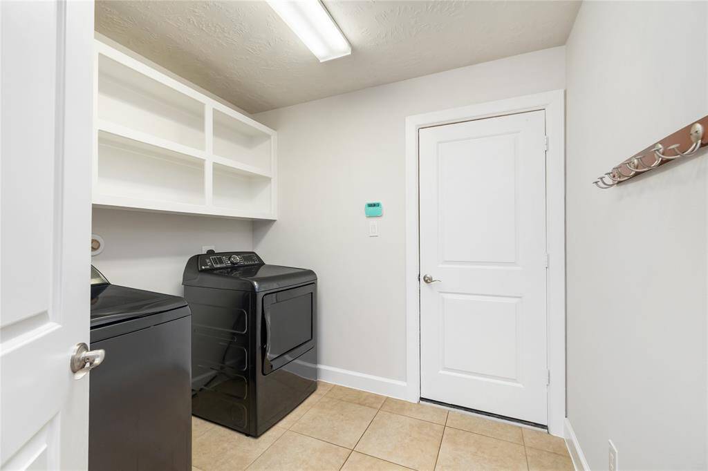 This spacious laundry room offers upper built-in shelving for convenient storage, tile flooring, and direct access to the garage.