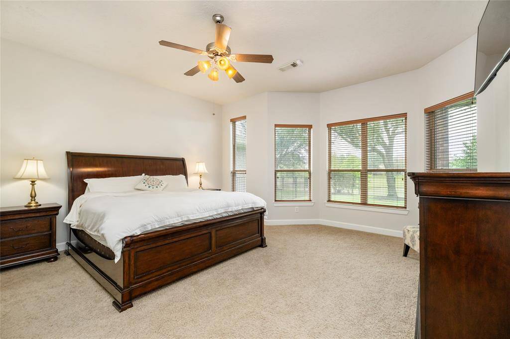The spacious primary suite features a serene bay window sitting area with peaceful lake views, plush carpeting, and abundant natural light. A tray ceiling with a ceiling fan adds comfort and elegance. Just off to the left, the private en suite bath offers the perfect space to unwind.