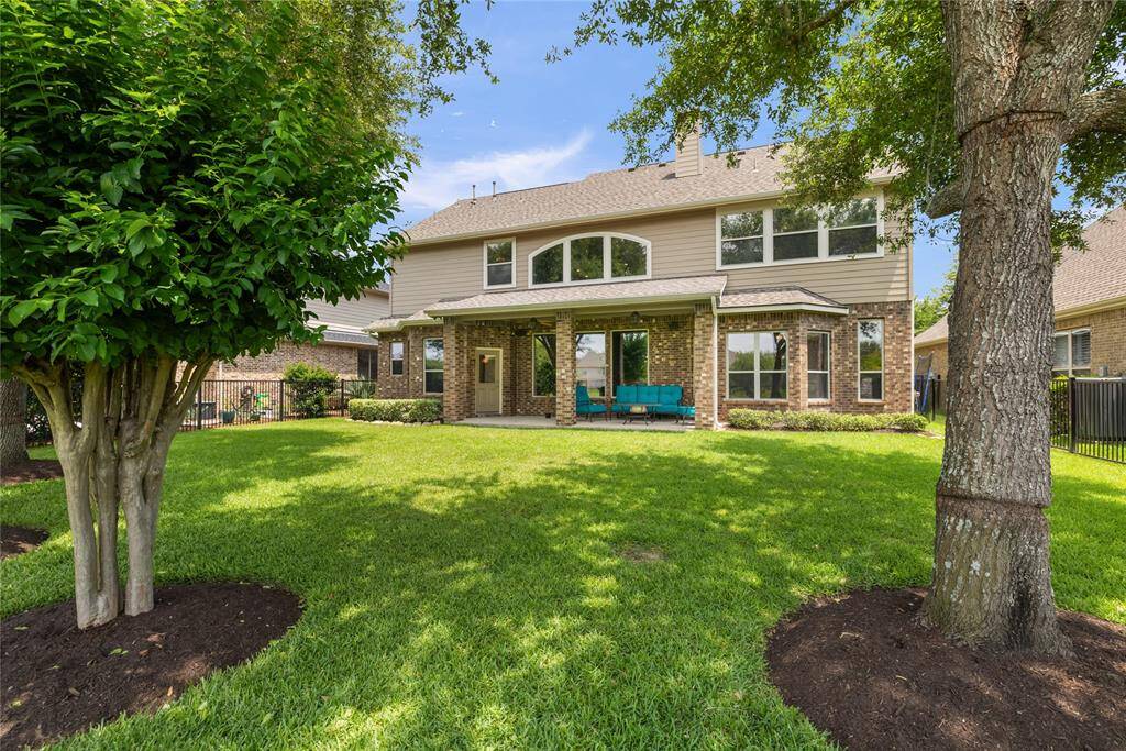 The beautifully manicured backyard offers a peaceful retreat with mature shade trees, lush lawn, and a covered patio perfect for relaxing or entertaining. Enjoy lake views just beyond the wrought iron fence—ideal for morning coffee or evening sunsets in your own private oasis.