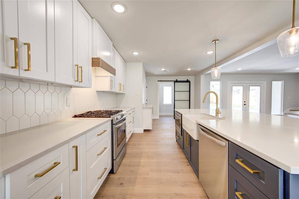 The 23x16 island kitchen is a chef’s dream, featuring quartz countertops, white cabinetry, and stainless steel appliances, including a gas range. A decorative backsplash and barn door pantry add character, while the breakfast bar provides additional seating.