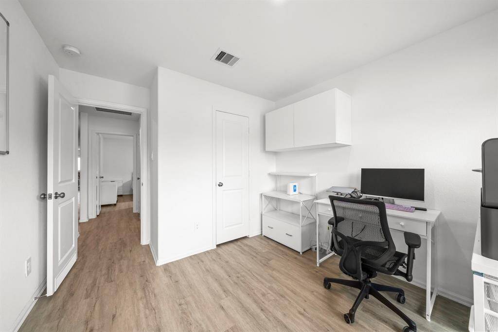 This home office or flex space features bright white walls and wood-look flooring, creating a clean and modern work environment.