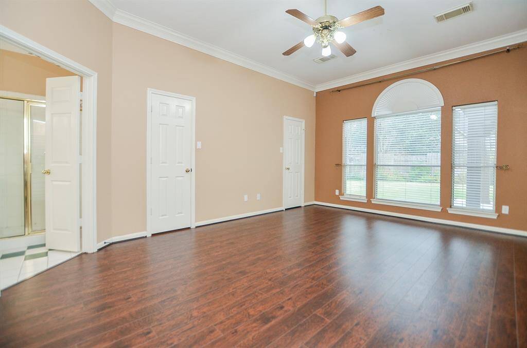 Your divine primary suite --- your personal, private place of peace and repose --- features gorgeous wood floors, wall-wide arched windows, high ceiling and crown molding topping off neutral earth tones on the walls. (Peeking out, left, is your ensuite bath.)