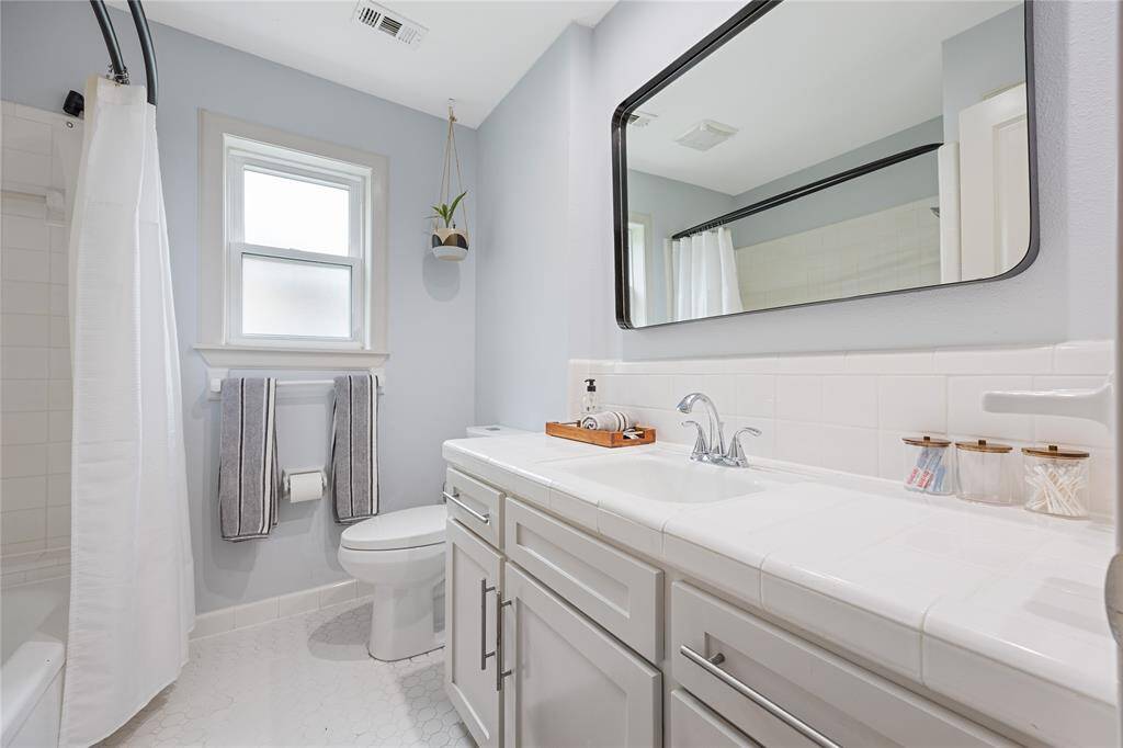 Full Guest Bathroom with Updated Fixtures and Natural LightBright, functional guest bath with tile countertops, framed mirror, soft-close vanity, and hex tile flooring. A clean and inviting space for visitors.