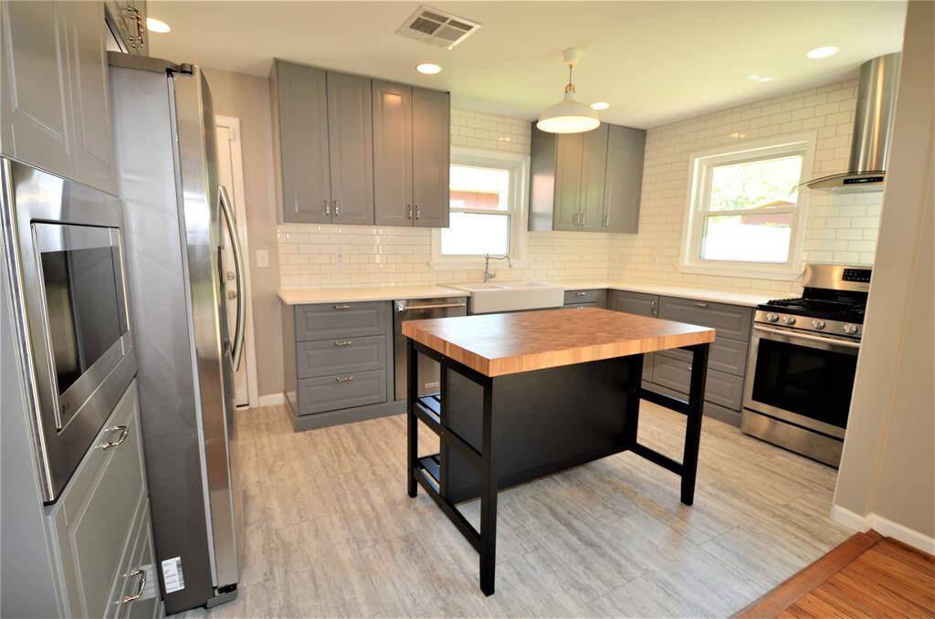Tons of details in this kitchen features: white sparkling quartz countertops, white subway backsplash wall tile, stylish sink with faucet, elegant butcher block island, stainless steel appliances and floor tile.