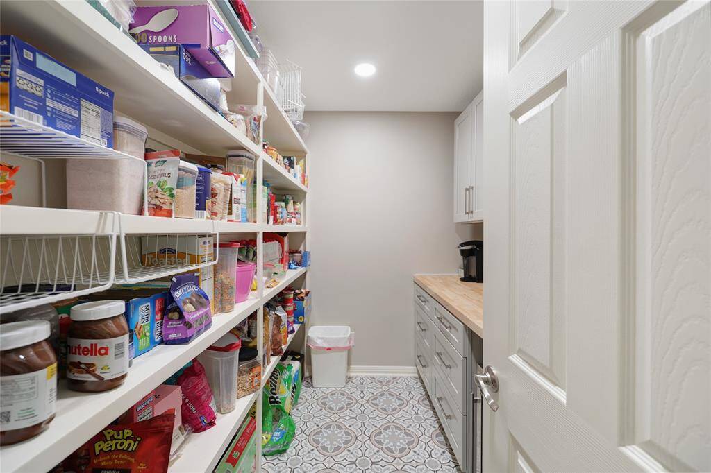 An entertainer’s dream pantry, this space boasts deep built-in shelves, decorative tile flooring, and a long butcher-block countertop perfect for a coffee station. Abundant storage ensures every grocery trip has a home, and even includes space for a wine fridge.