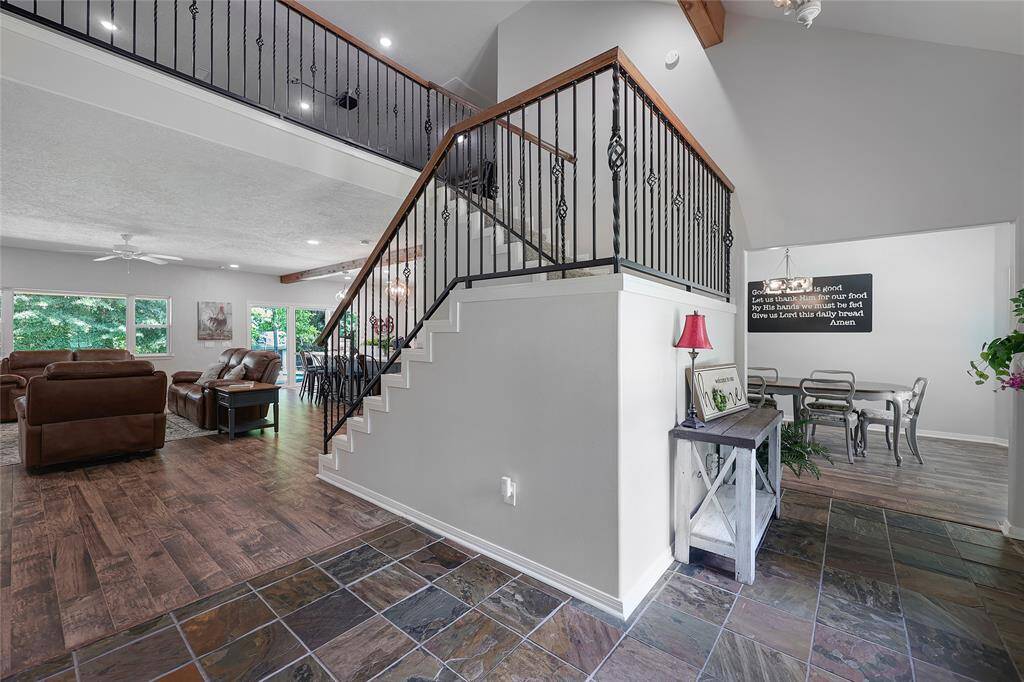 The entryway impresses with rich slate tile flooring, an open-concept staircase with wrought-iron balusters, and soaring ceilings. Natural light flows through the home from multiple directions, guiding you into the heart of the living space while offering peeks into the formal dining area and upstairs game room.
