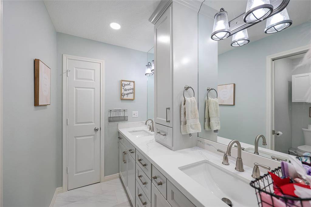 This stylish bathroom features a modern double-sink vanity with shaker-style cabinetry, a quartz countertop, and brushed nickel hardware. A tall central cabinet offers excellent storage.